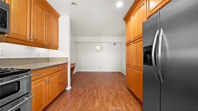 kitchen with recessed lighting, stainless steel appliances, light wood-type flooring, light stone countertops, and brown cabinetry