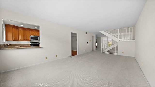 unfurnished living room featuring stairway, recessed lighting, a sink, and light colored carpet