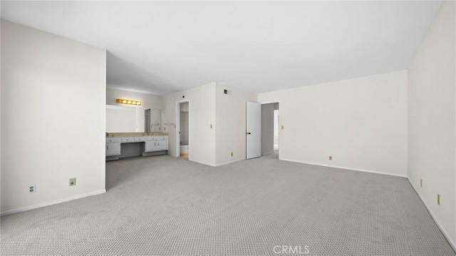 unfurnished living room featuring light carpet, built in desk, and baseboards