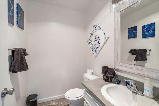 half bathroom featuring toilet, baseboards, wood finished floors, and vanity