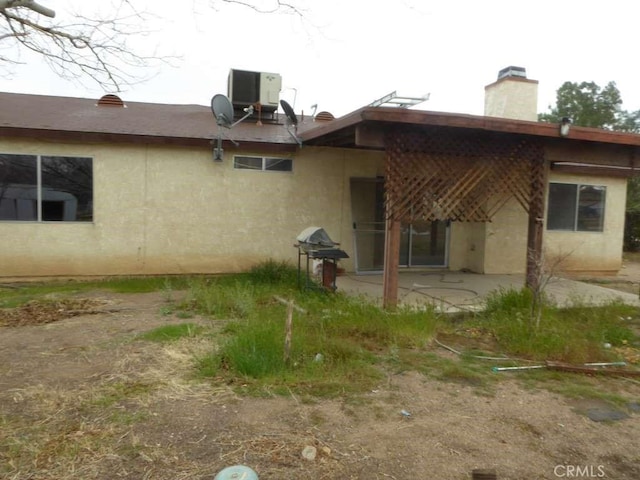 rear view of house featuring cooling unit, a patio area, a chimney, and stucco siding