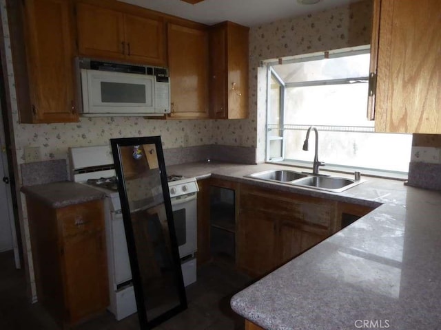 kitchen with white appliances, light countertops, a sink, and wallpapered walls