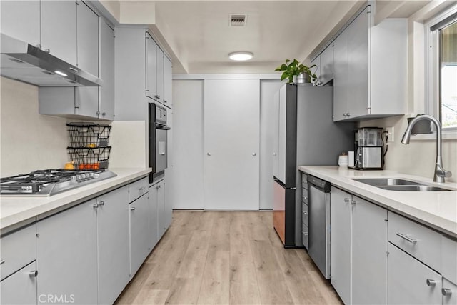 kitchen featuring visible vents, a sink, under cabinet range hood, appliances with stainless steel finishes, and light wood-type flooring