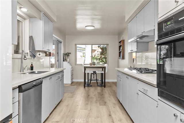 kitchen with a sink, stainless steel appliances, light countertops, under cabinet range hood, and tasteful backsplash