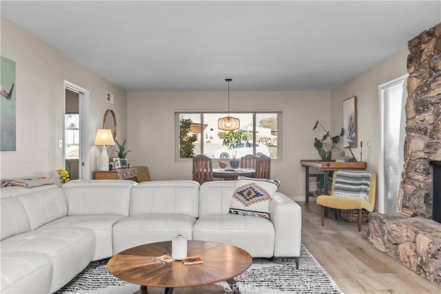 living area featuring a stone fireplace, visible vents, and light wood finished floors