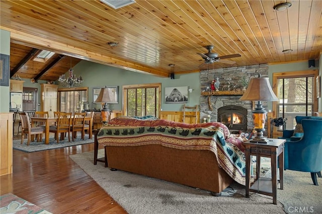 living room with a ceiling fan, lofted ceiling, wooden ceiling, wood finished floors, and a stone fireplace