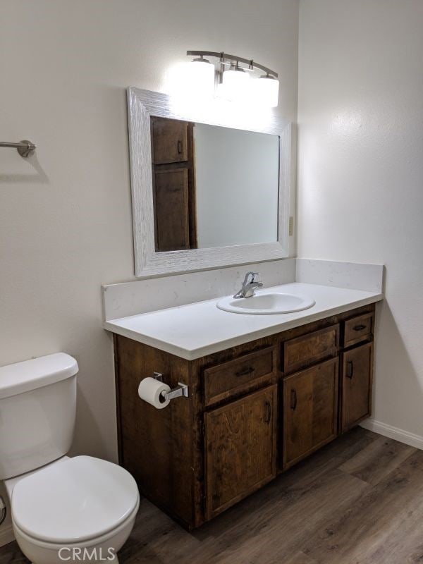 half bathroom with toilet, baseboards, wood finished floors, and vanity