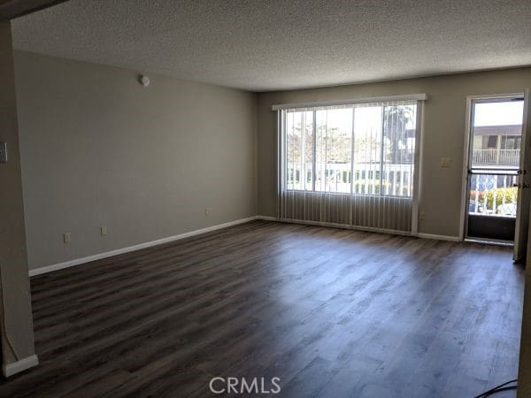 empty room with dark wood-type flooring, a healthy amount of sunlight, and baseboards