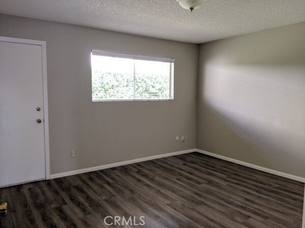 empty room with a textured ceiling, dark wood finished floors, and baseboards