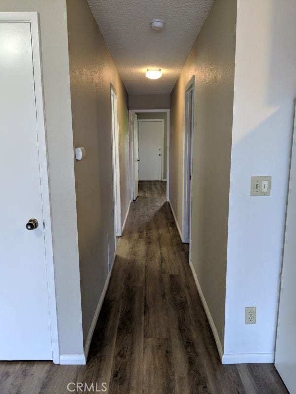 hall featuring dark wood-style floors, baseboards, and a textured ceiling