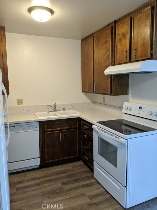 kitchen with dark wood-style floors, light countertops, a sink, white appliances, and under cabinet range hood