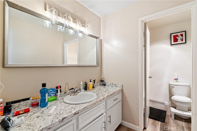 bathroom featuring toilet, wood finished floors, vanity, and baseboards