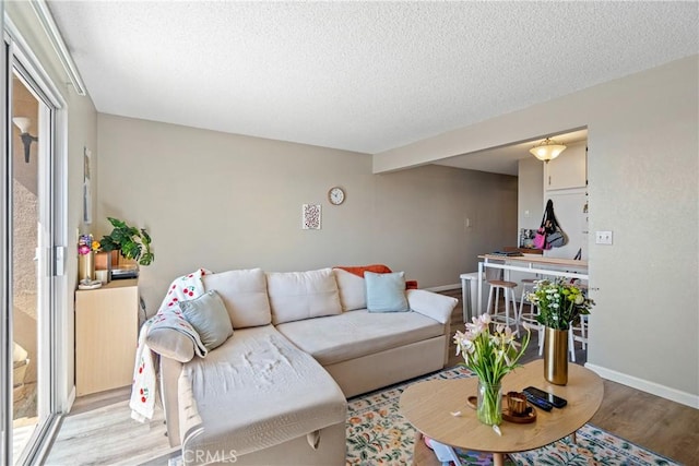 living room with a textured ceiling, light wood finished floors, and baseboards