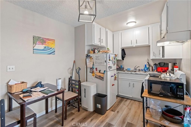 kitchen with light wood finished floors, freestanding refrigerator, a sink, a textured ceiling, and black microwave