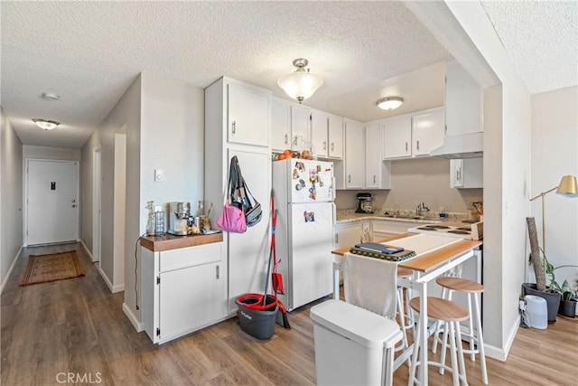 kitchen with white cabinets, wood finished floors, freestanding refrigerator, a textured ceiling, and a sink