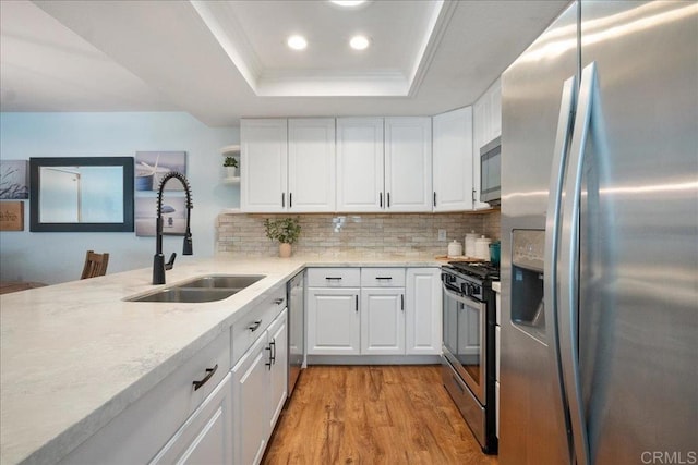 kitchen featuring stainless steel appliances, a raised ceiling, white cabinets, a sink, and light wood-type flooring