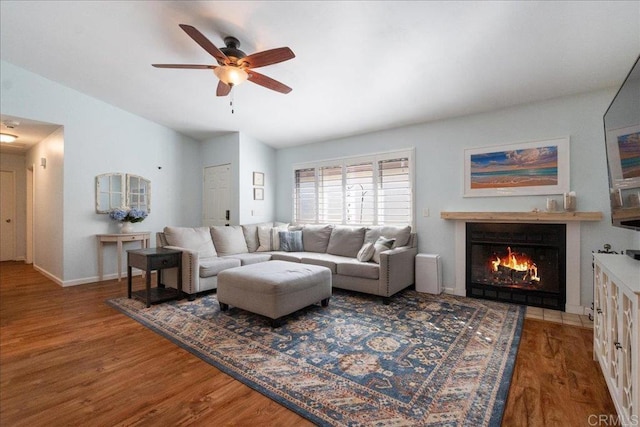 living area featuring lofted ceiling, a lit fireplace, ceiling fan, and wood finished floors