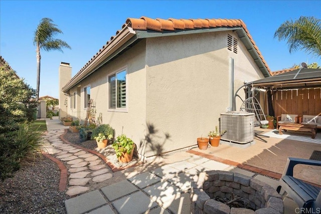 exterior space with central AC unit, an outdoor living space with a fire pit, a tile roof, a patio area, and stucco siding