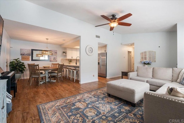 living area featuring lofted ceiling, visible vents, baseboards, and wood finished floors