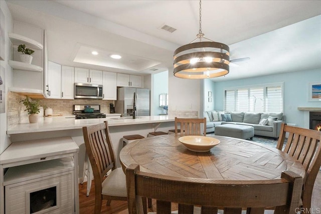 dining space with visible vents, a lit fireplace, a tray ceiling, a notable chandelier, and recessed lighting