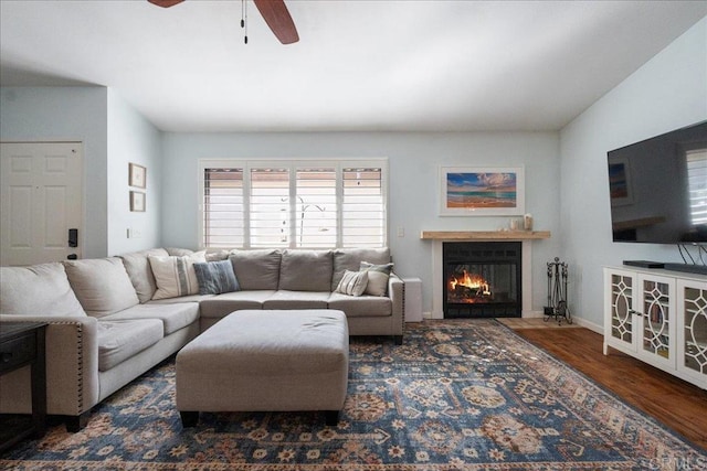 living area with a glass covered fireplace, wood finished floors, and a ceiling fan