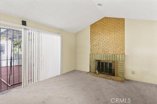 unfurnished living room with vaulted ceiling, a textured ceiling, a brick fireplace, and carpet