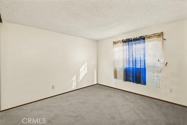 empty room featuring a textured ceiling, carpet, and baseboards