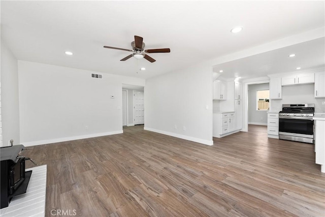 unfurnished living room with visible vents, recessed lighting, a wood stove, and wood finished floors