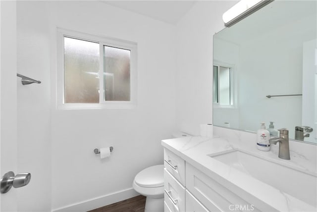 half bath featuring toilet, vanity, baseboards, and wood finished floors