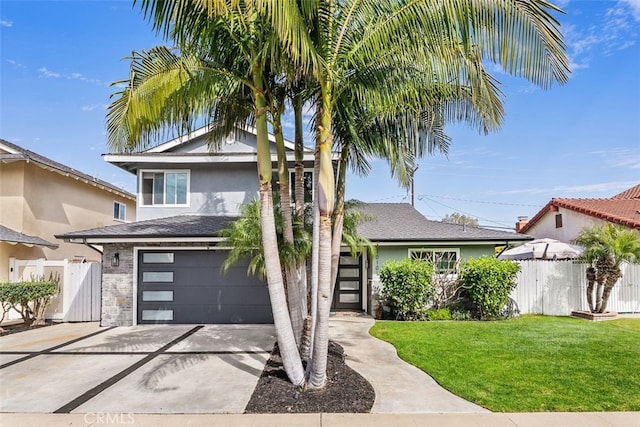 view of front of house with stucco siding, concrete driveway, a front yard, fence, and a garage