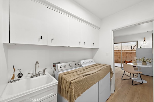 clothes washing area with cabinet space, separate washer and dryer, a sink, and light wood finished floors