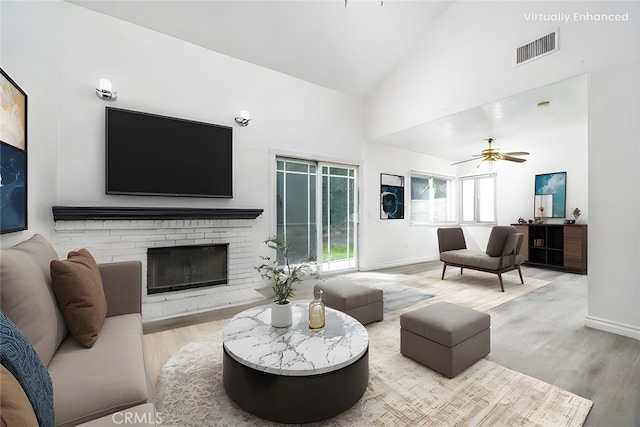 living room featuring visible vents, a ceiling fan, wood finished floors, a brick fireplace, and high vaulted ceiling