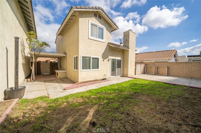 back of property with a yard, a chimney, a patio, stucco siding, and fence