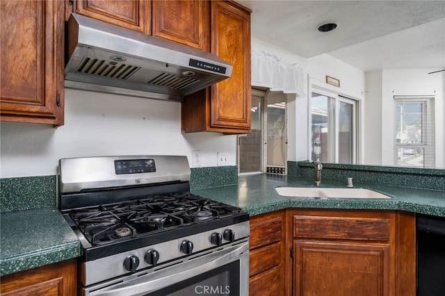 kitchen featuring dark countertops, a sink, gas range, dishwasher, and under cabinet range hood