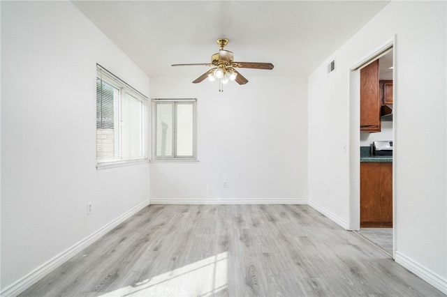 spare room with a ceiling fan, light wood-type flooring, visible vents, and baseboards