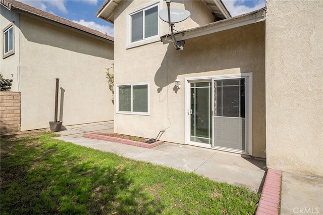 rear view of property featuring a patio, a yard, and stucco siding