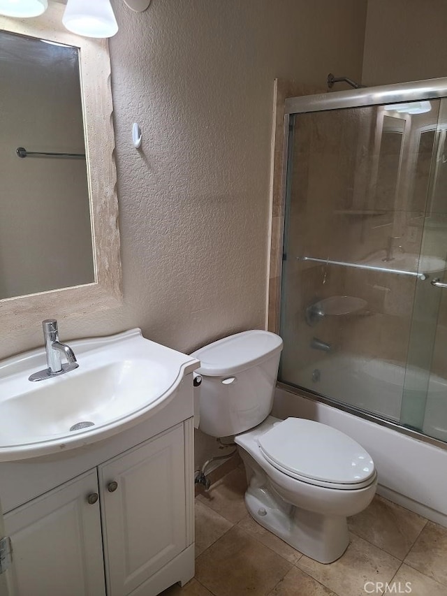 full bath with a textured wall, toilet, shower / bath combination with glass door, vanity, and tile patterned floors