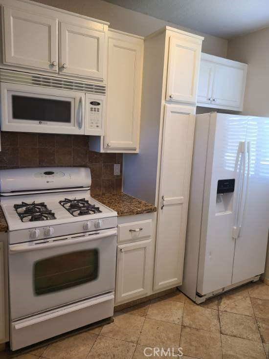 kitchen featuring light tile patterned floors, white appliances, white cabinetry, backsplash, and dark stone countertops