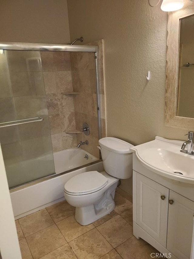 full bathroom featuring a textured wall, toilet, shower / bath combination with glass door, tile patterned flooring, and vanity