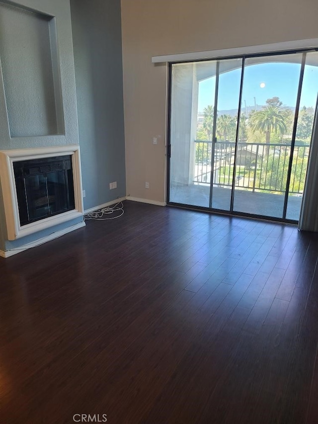 unfurnished living room featuring a glass covered fireplace, dark wood-style flooring, and baseboards