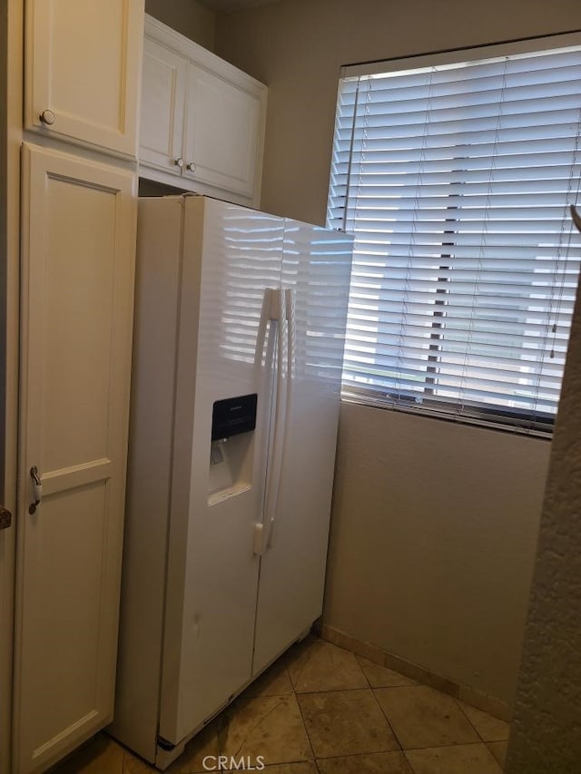 kitchen with white refrigerator with ice dispenser, white cabinetry, and light tile patterned floors