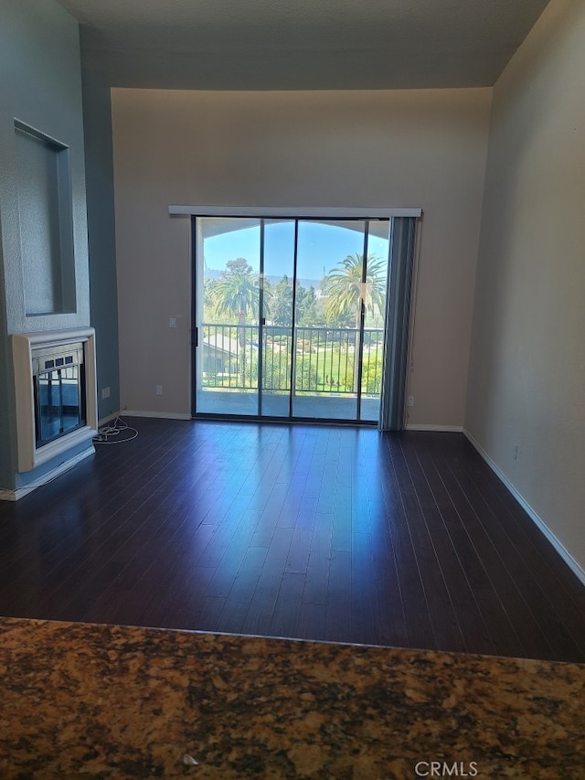 unfurnished living room featuring baseboards, dark wood-type flooring, and a glass covered fireplace