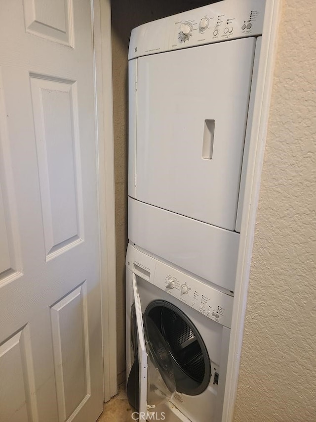 laundry room with a textured wall, laundry area, and stacked washer / drying machine