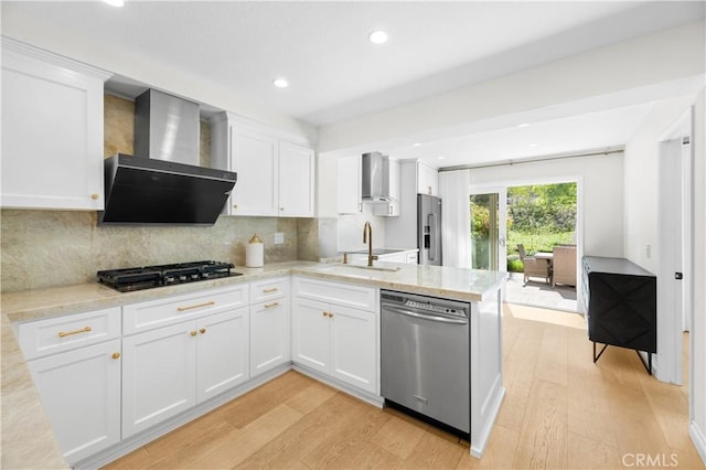 kitchen with wall chimney range hood, light wood-type flooring, a sink, and appliances with stainless steel finishes