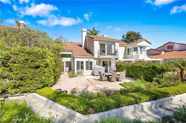 rear view of property with a patio, a balcony, a tile roof, a chimney, and stucco siding