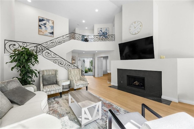 living room featuring baseboards, a fireplace with flush hearth, stairway, wood finished floors, and a high ceiling