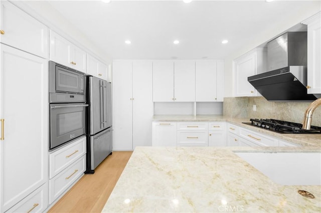 kitchen featuring white cabinets, wall chimney range hood, appliances with stainless steel finishes, and light stone countertops