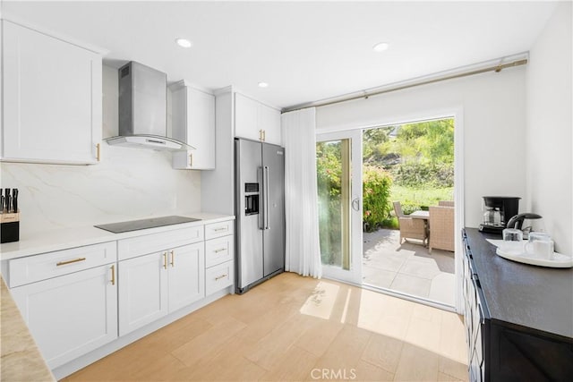 kitchen with black electric stovetop, backsplash, white cabinets, high quality fridge, and wall chimney exhaust hood