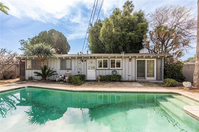 rear view of property featuring board and batten siding, fence, and a fenced in pool