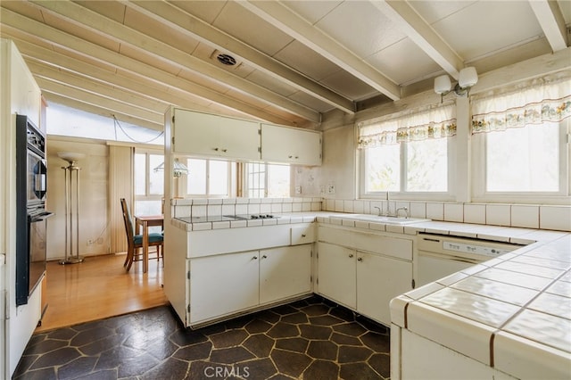 kitchen featuring lofted ceiling with beams, white dishwasher, a sink, and tile counters